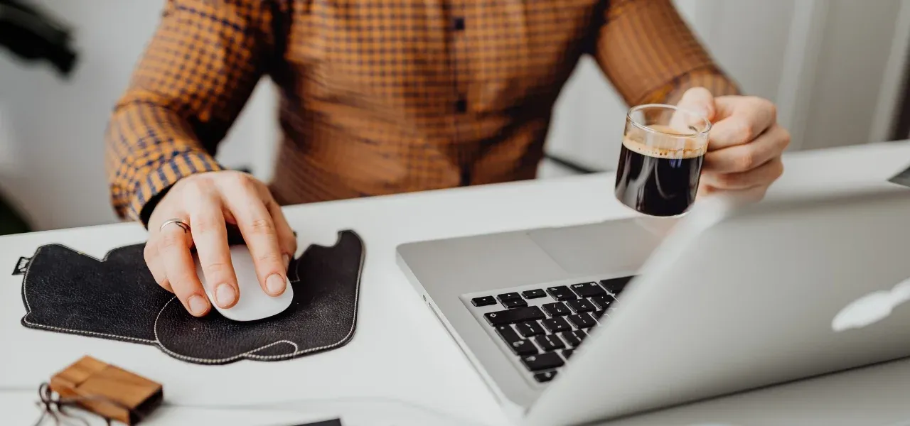 Millennial professional working on a laptop at a desk while holding a small cup of coffee in a modern workspace.
