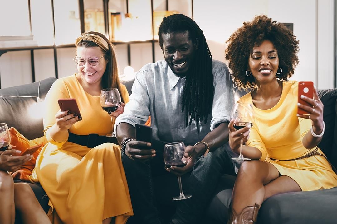 a group of people of different ages sitting together at a table looking at their phones drinking a glass of wine