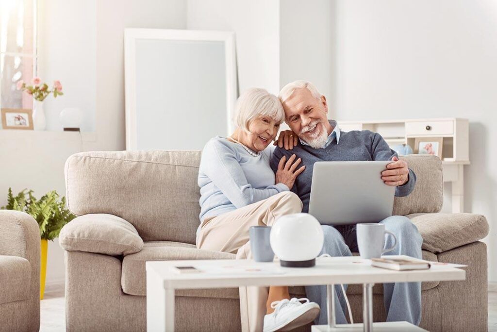 an older couple sitting on a couch joyfully looking at a computer together