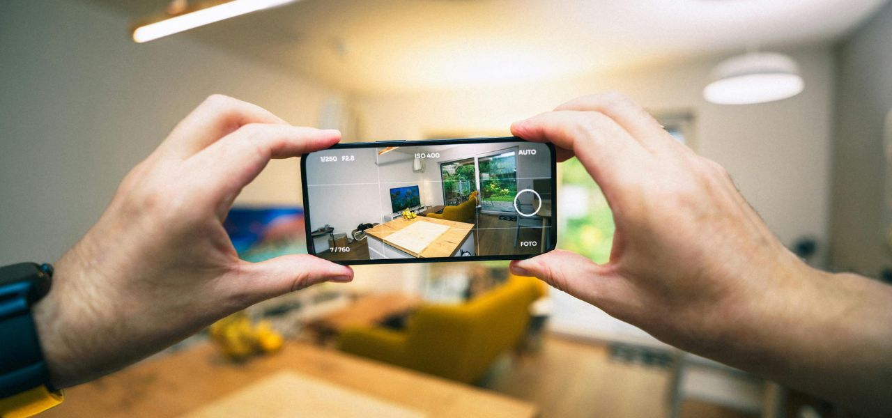 Hands holding a smartphone while recording video of a modern living room interior.